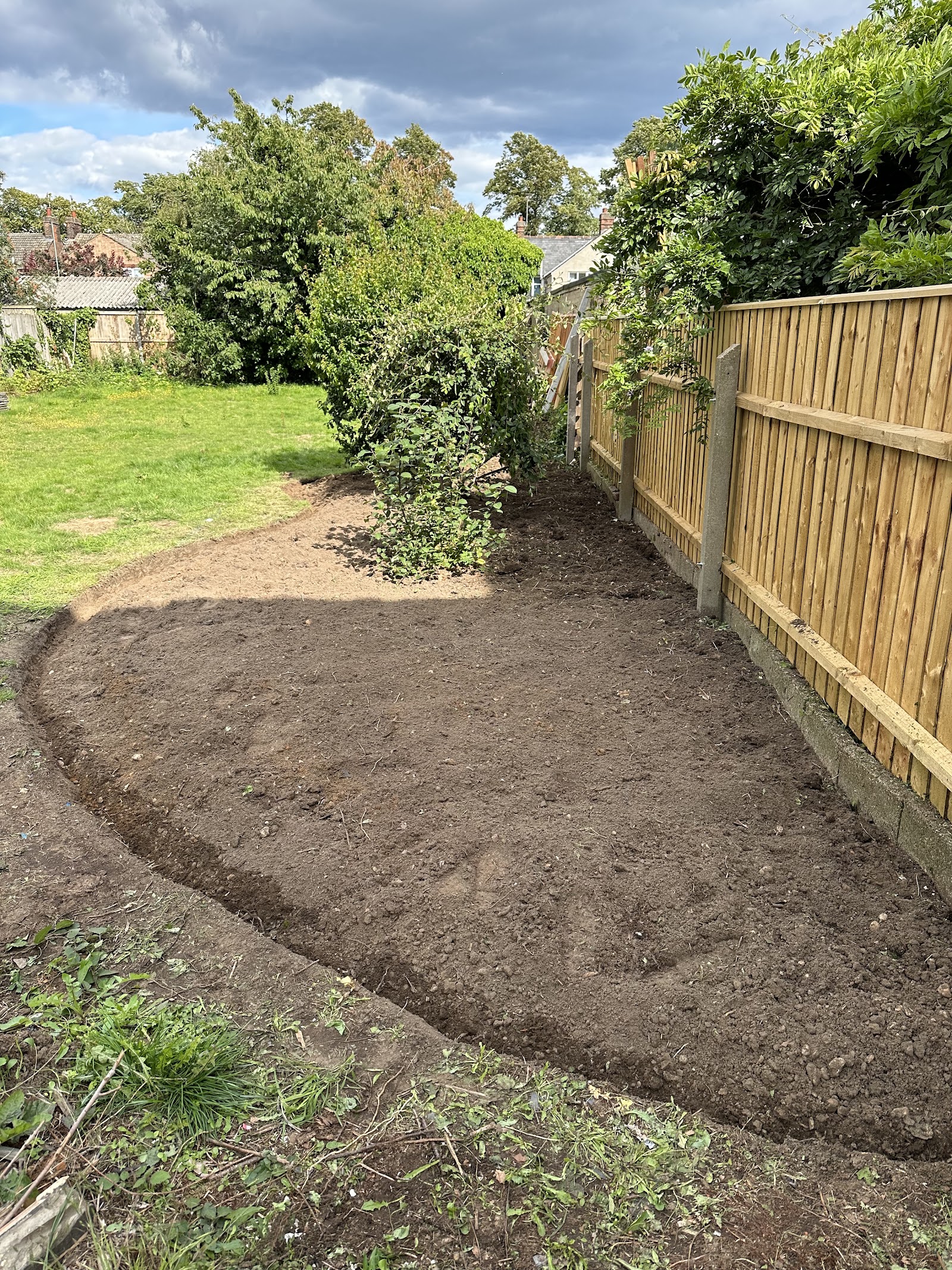 A garden border fully cleared of overgrowth against a new fence